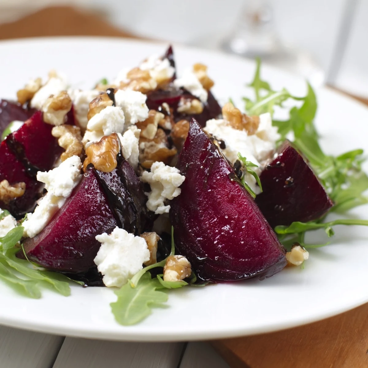 Vibrant roasted beet goat cheese salad with arugula, walnuts, and a tangy balsamic vinaigrette on a white plate.