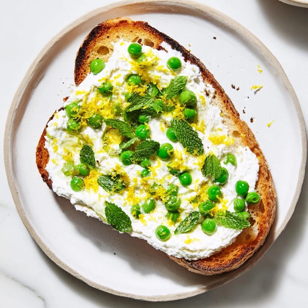 A vibrant slice of pea & mint ricotta toast served with lemon wedges for a bright, tangy finish.