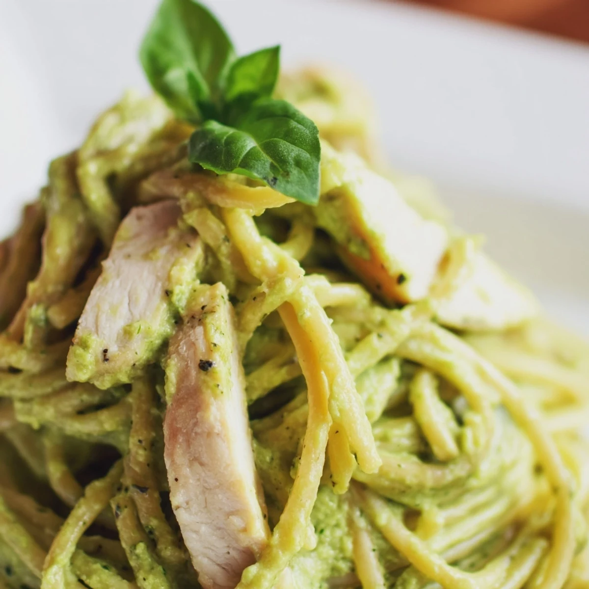 Ready-to-serve creamy avocado chicken pasta garnished with lemon zest and Parmesan on a rustic wooden table.