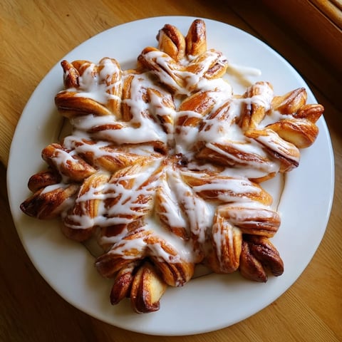 Golden, baked cinnamon roll pull-apart snowflake with soft dough and vanilla icing drizzle, a winter treat.