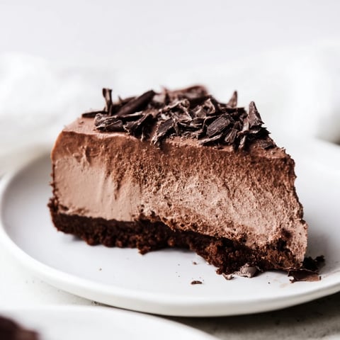A slice of Lighter Chocolate Cottage Cheese Cheesecake on a plate with dark chocolate shavings and fresh berries, showcasing its rich, creamy texture and crackly top.