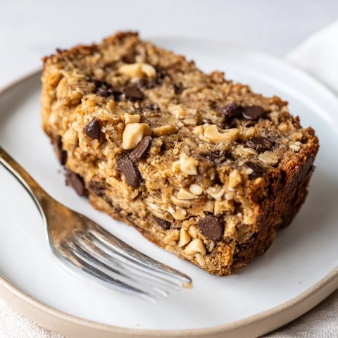 A thick slice of Chocolate Chip Peanut Butter Oatmeal Banana Bread on a rustic wooden board, with melty chocolate chips and peanut crumbles on top.