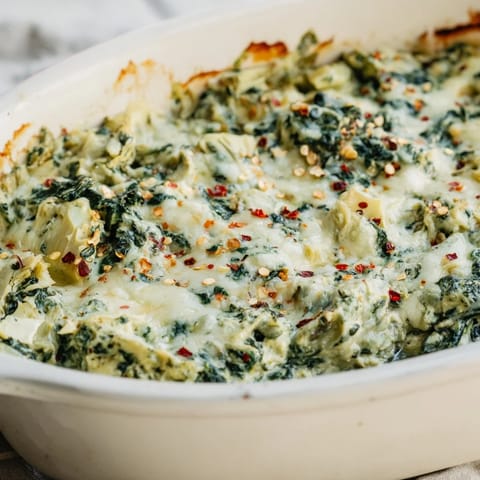 A close-up shot of creamy Warm Spinach and Artichoke Dip, garnished with Parmesan cheese and herbs.