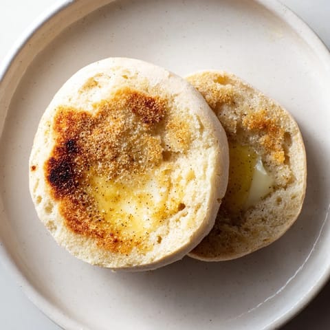 Freshly baked sheet pan English muffins dusted with cornmeal, ready to be toasted and enjoyed.