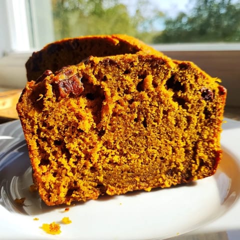 A golden-brown pumpkin bread loaf is cooled on a wire rack, its top crackled and lightly dusted with cinnamon sugar, ready to slice.