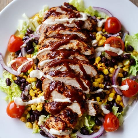 Sliced smoky BBQ chicken rests on fresh romaine with corn, black beans, and tomatoes in ranch.
