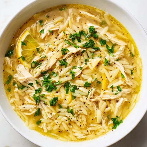 A close-up of Lemon Pepper Chicken Orzo Soup shows al dente orzo in a savory broth with lemon wedges.