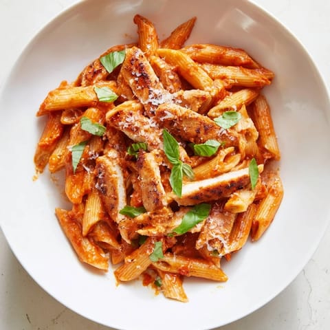 The close-up photo of Spicy Tomato Chicken Pasta highlights the glossy sauce clinging to al dente penne, with juicy chicken strips and a sprinkle of Parmesan cheese.  