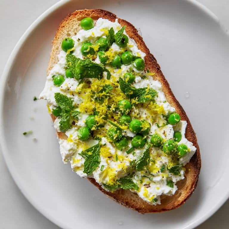 Whipped ricotta, sweet peas, and fresh mint spread thickly over crunchy sourdough, perfect for a light brunch.