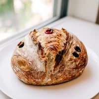 A detailed view of a freshly baked turkey-shaped sourdough loaf, its golden crust dusted with seeds to mimic feathers, ready for a festive holiday table.