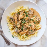 Golden-brown chicken strips and sautéed cremini mushrooms swim in a creamy paprika sauce, all piled high on buttery egg noodles for a comforting dinner.