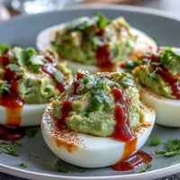 Creamy avocado deviled eggs with a spicy Sriracha drizzle, perfect for healthy appetizers or party snacks.